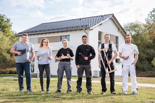 Auszubildende verschiedener Berufe stehen vor einem Finger-Haus und stellen sich vor. 